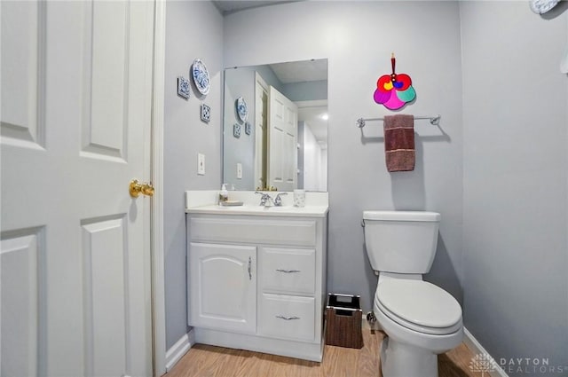 half bath with toilet, baseboards, wood finished floors, and vanity
