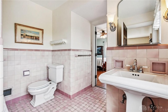 bathroom featuring tile walls, ceiling fan, wainscoting, and toilet