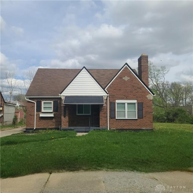 view of front of home featuring a chimney, a front yard, and brick siding