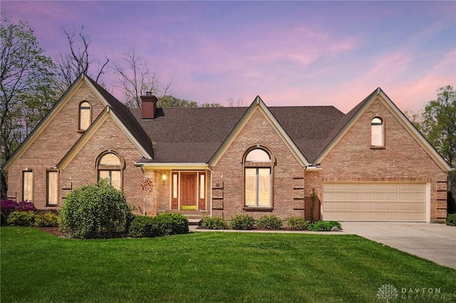 french country home featuring brick siding, a yard, driveway, and a chimney