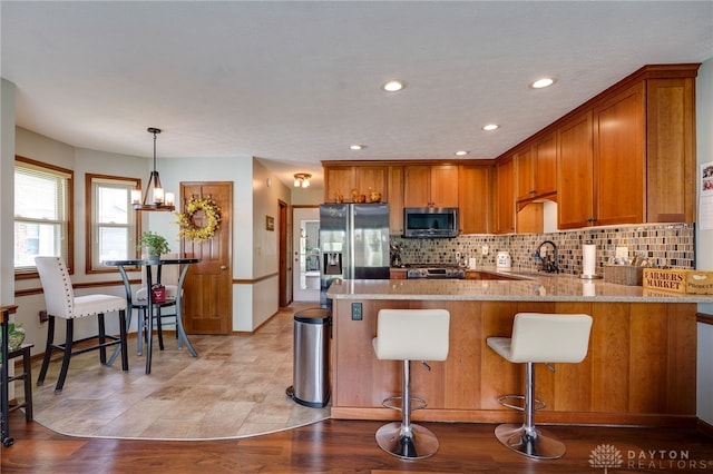 717 Walden Way, Dayton, OH 45440 - kitchen with a peninsula, brown cabinetry, light stone countertops, appliances with stainless steel finishes, and tasteful backsplash