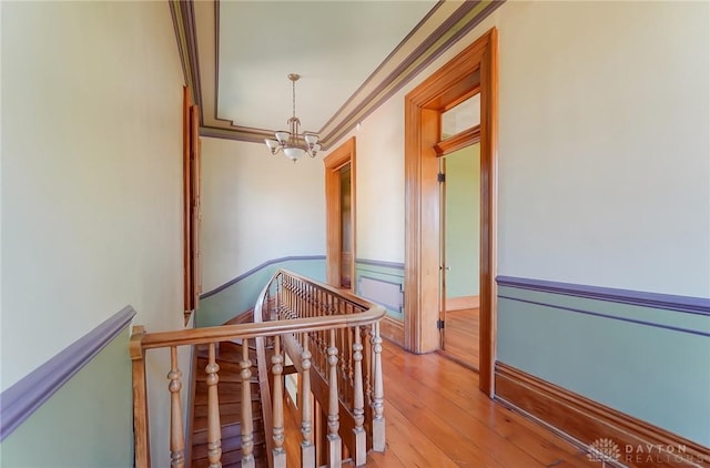 hall featuring an inviting chandelier, crown molding, light wood-style flooring, and an upstairs landing