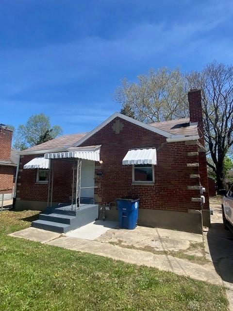 view of side of home featuring brick siding, a chimney, and a patio