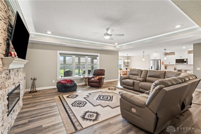 838 W Bentley Cir, Troy, OH 45373 - living room with ceiling fan with notable chandelier, wood finished floors, a raised ceiling, and a fireplace
