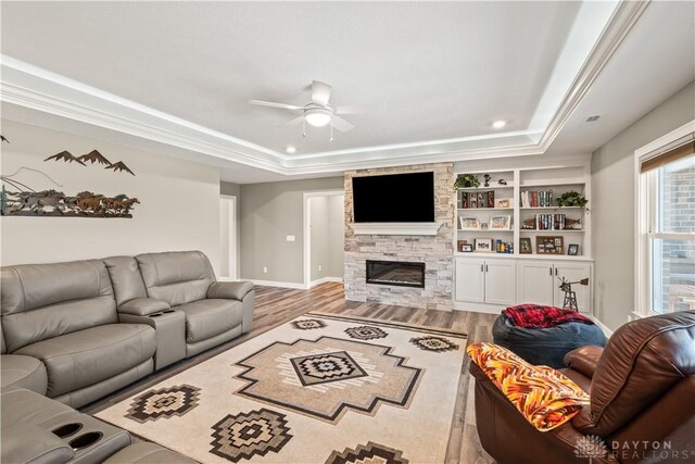 838 W Bentley Cir, Troy, OH 45373 - living room featuring a ceiling fan, a tray ceiling, a stone fireplace, and wood finished floors