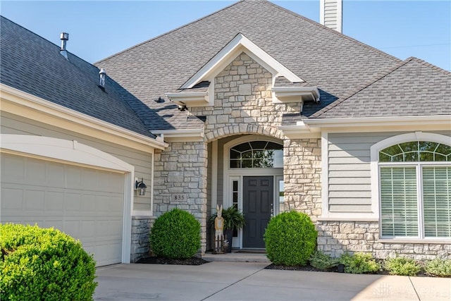 view of exterior entry featuring a shingled roof, driveway, and stone siding