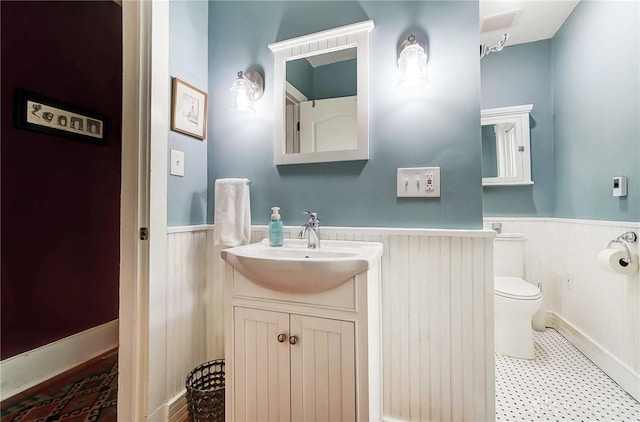 half bathroom featuring vanity, wainscoting, and toilet