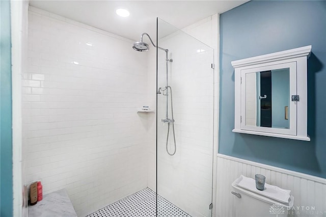 bathroom with wainscoting, a tile shower, and toilet