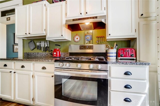 kitchen featuring dark stone counters, under cabinet range hood, stainless steel gas stove, and white cabinets