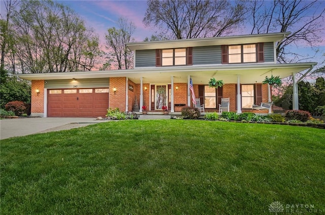 traditional-style house featuring covered porch, a lawn, brick siding, concrete driveway, and an attached garage