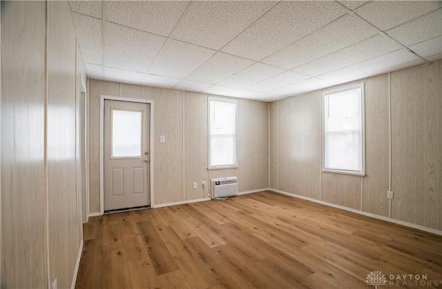 foyer featuring wood-type flooring, baseboards, a drop ceiling, and a wall unit AC