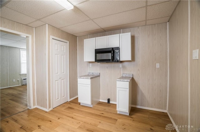 kitchen with light countertops, white cabinetry, black microwave, and a paneled ceiling