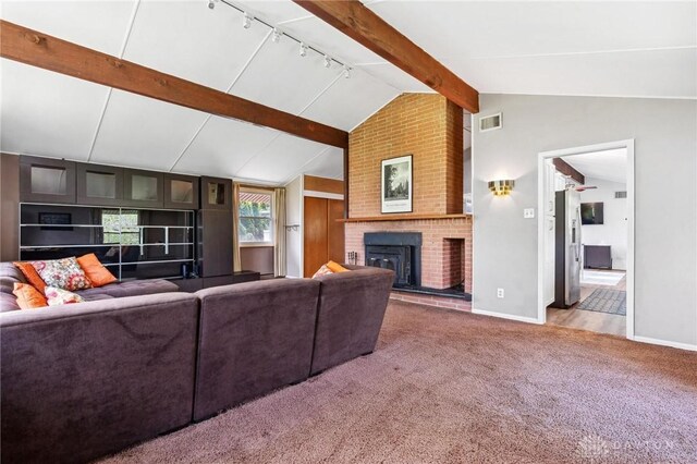 carpeted living room with visible vents, a brick fireplace, track lighting, baseboards, and lofted ceiling with beams