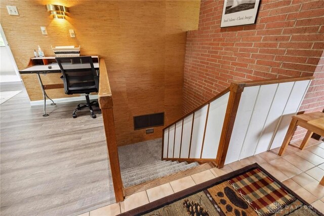 unfurnished office with brick wall, visible vents, and wood finished floors