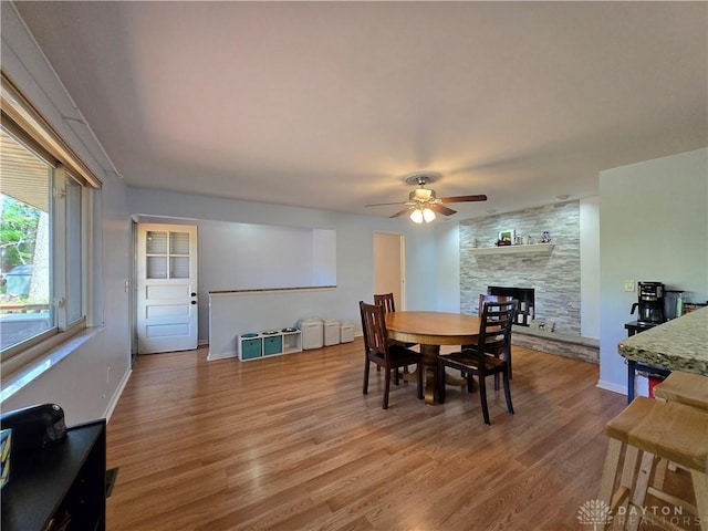 dining space featuring baseboards, a ceiling fan, wood finished floors, and a fireplace