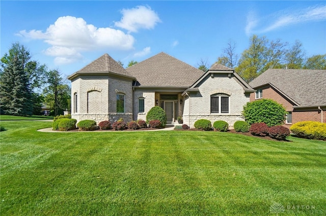 french country style house featuring brick siding, a shingled roof, and a front yard