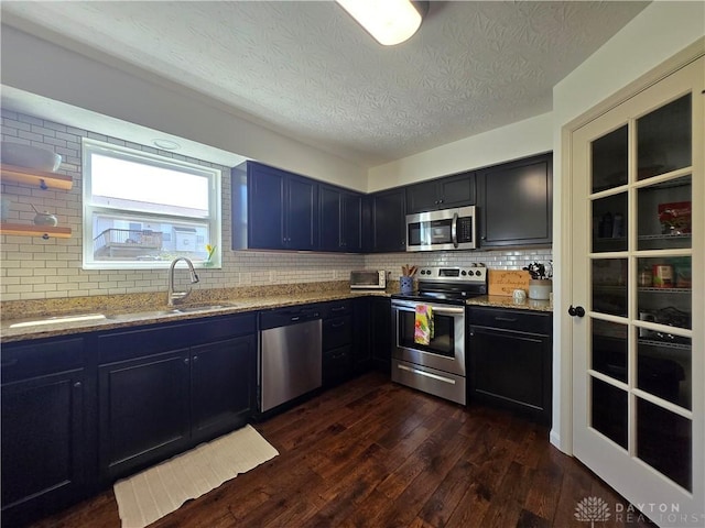 kitchen with light stone counters, a sink, stainless steel appliances, tasteful backsplash, and dark wood-type flooring