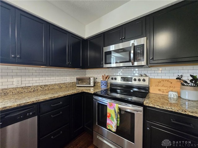 kitchen featuring light stone counters, appliances with stainless steel finishes, dark cabinets, and tasteful backsplash
