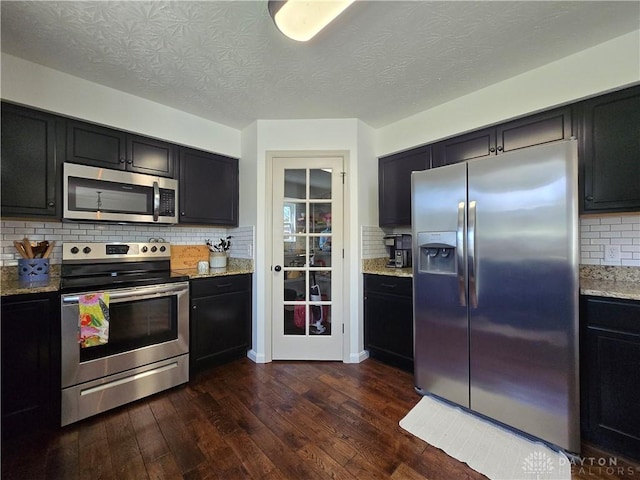 kitchen with dark wood-style flooring, appliances with stainless steel finishes, decorative backsplash, and light stone counters