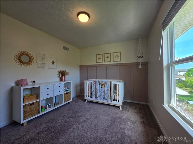 bedroom featuring visible vents, baseboards, a crib, a textured ceiling, and carpet flooring