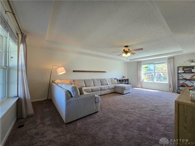 carpeted living room with a raised ceiling, ceiling fan, baseboards, and visible vents