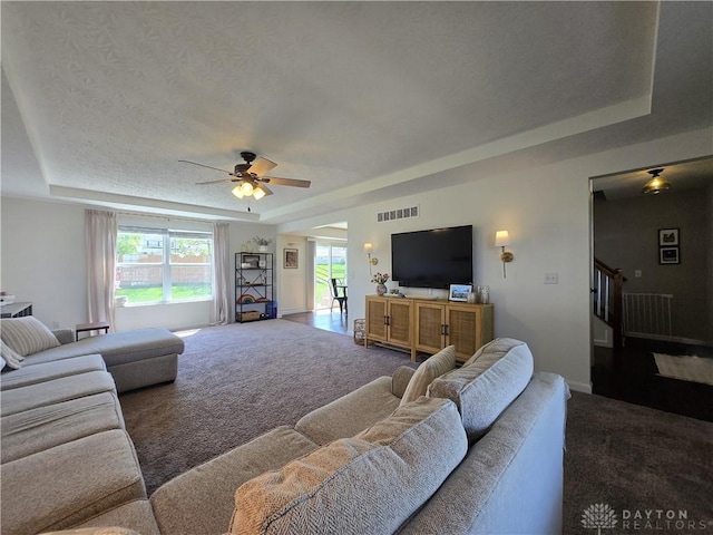living area with visible vents, carpet flooring, a raised ceiling, and ceiling fan