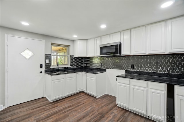 kitchen featuring dark wood-style flooring, dark countertops, a sink, stainless steel microwave, and backsplash