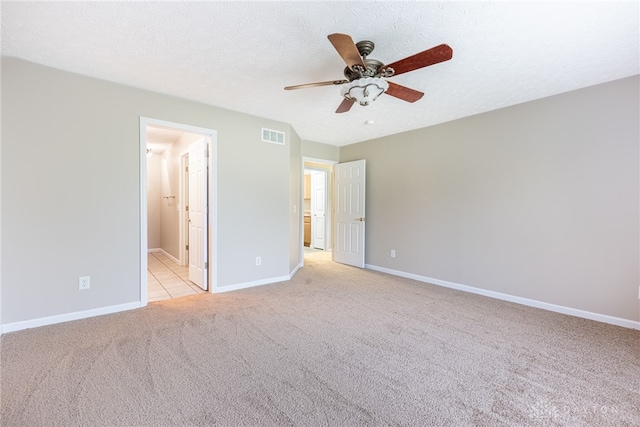 unfurnished bedroom with ceiling fan, light colored carpet, visible vents, baseboards, and ensuite bath
