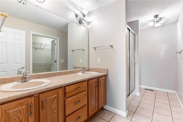 full bathroom featuring tile patterned flooring, a sink, a textured ceiling, and a shower stall