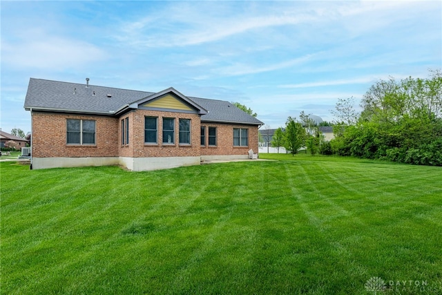 rear view of property featuring roof with shingles, a yard, and brick siding