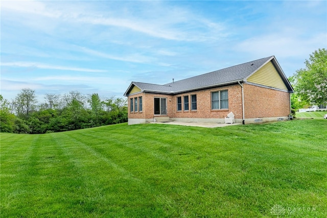 back of property featuring a lawn, a patio area, roof with shingles, and brick siding