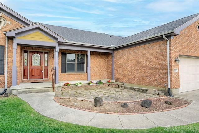 view of exterior entry featuring brick siding, roof with shingles, and a garage