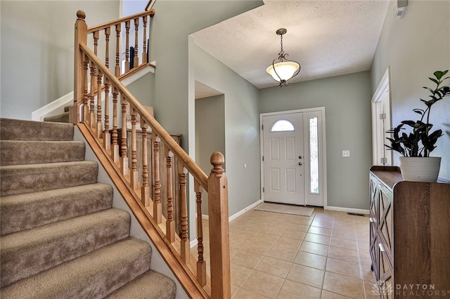 entrance foyer featuring a textured ceiling, baseboards, light tile patterned floors, and stairway