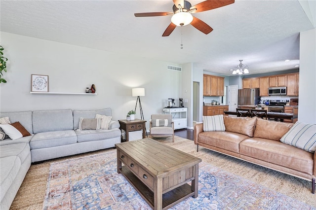 living room with visible vents, a textured ceiling, and ceiling fan with notable chandelier