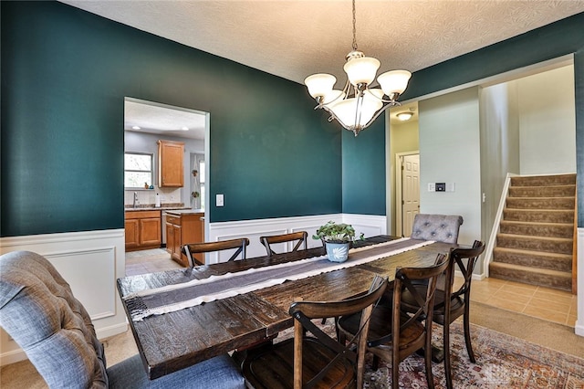 dining room featuring an inviting chandelier, a wainscoted wall, stairway, and light tile patterned flooring