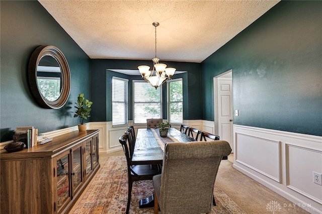 dining area featuring a textured ceiling, wainscoting, a decorative wall, and a notable chandelier
