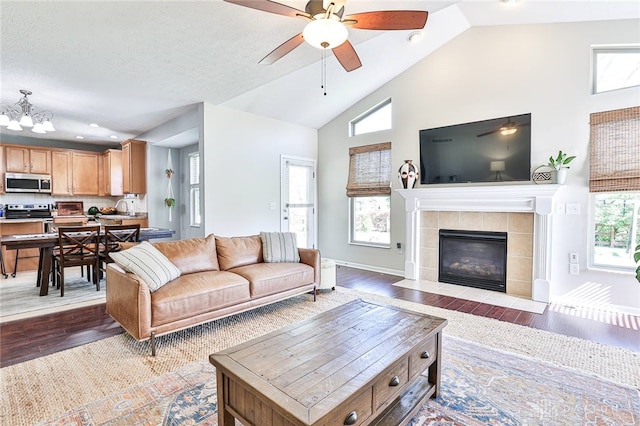 living area featuring dark wood finished floors, ceiling fan with notable chandelier, high vaulted ceiling, and a fireplace