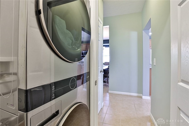 laundry area with laundry area, stacked washer and clothes dryer, baseboards, and light tile patterned flooring