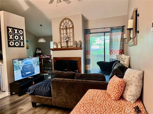 living area featuring a ceiling fan, vaulted ceiling, wood finished floors, and a fireplace