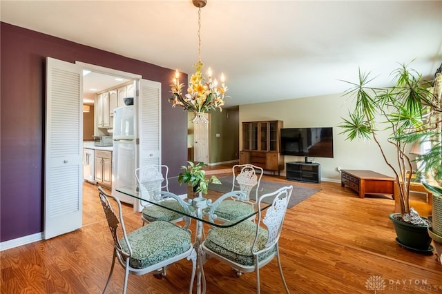 dining area with baseboards, an inviting chandelier, and light wood-style flooring