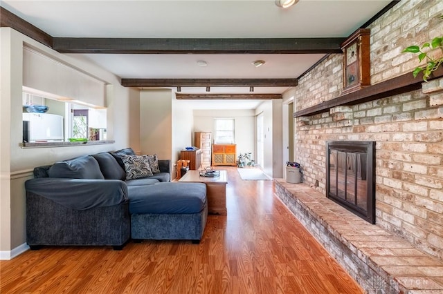 living area with a brick fireplace, light wood-type flooring, and beam ceiling