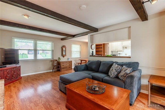 living area featuring baseboards, light wood-style flooring, and beam ceiling