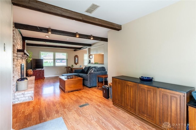 living room with light wood-style floors, beamed ceiling, a fireplace, and visible vents
