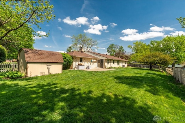 rear view of property featuring a storage unit, an outdoor structure, a fenced backyard, a lawn, and a patio