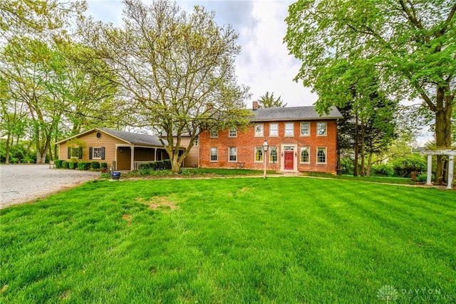 view of front of house featuring brick siding, a chimney, a front yard, and gravel driveway