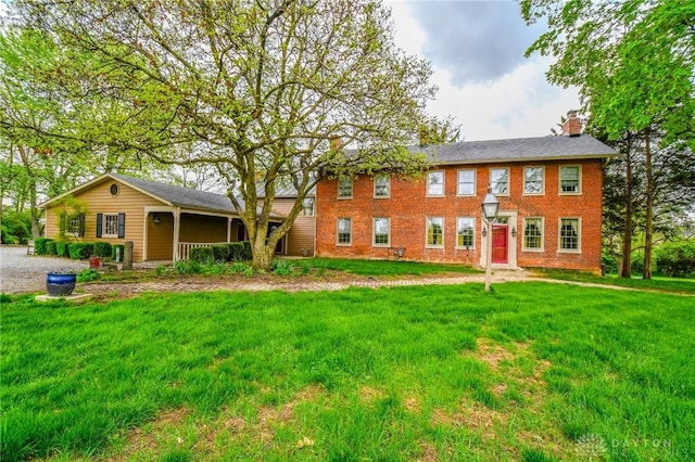 colonial home featuring a chimney, brick siding, and a front lawn