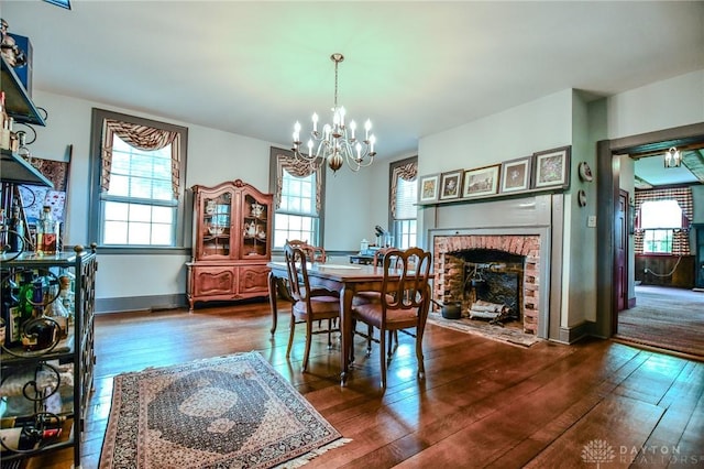 dining area with a wealth of natural light, dark wood-style flooring, a fireplace, and a notable chandelier