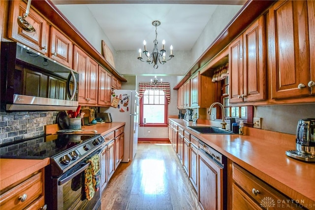 kitchen with freestanding refrigerator, a notable chandelier, a sink, dishwashing machine, and electric range
