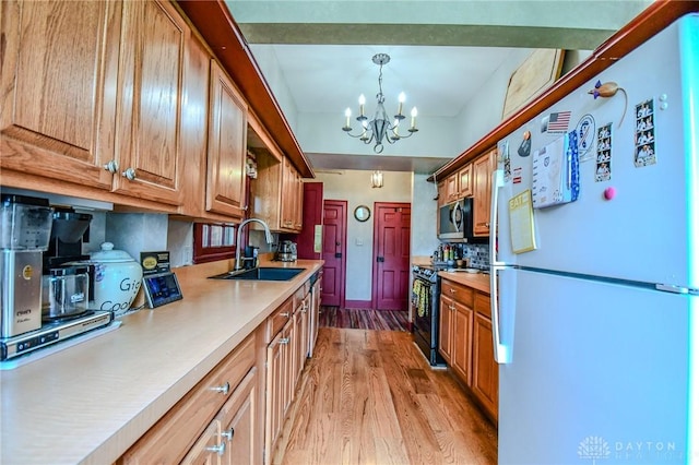 kitchen featuring a notable chandelier, light wood-style flooring, stainless steel appliances, a sink, and light countertops