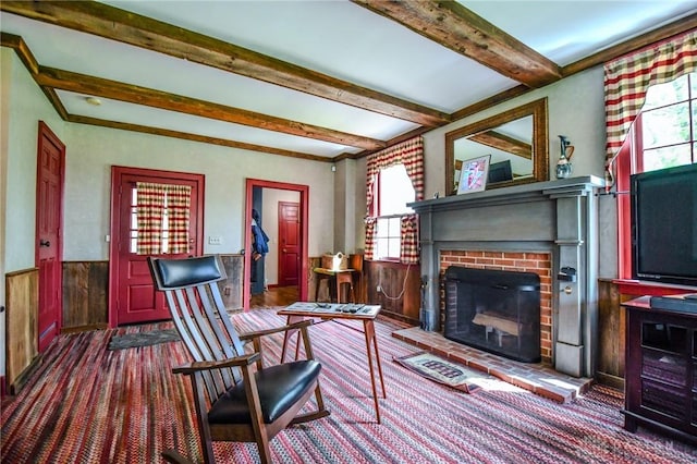 living room featuring carpet flooring, beam ceiling, wainscoting, and a brick fireplace